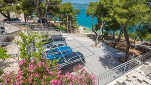A parking area with cars, surrounded by trees and overlooking a beach. - Apartment Villa Rosea (Split)