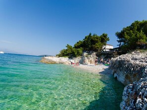 Un paysage côtier avec une eau turquoise et limpide, des rivages rocheux et un bâtiment bordé d’arbres sur la droite.