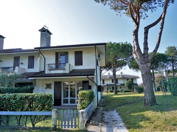 Traditional two-story home with a balcony, glass entrance, and chimney, set amidst well-maintained gardens.