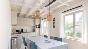 Una cocina moderna con armarios blancos, una mesa de comedor con sillas azules y un ventanal con cortinas.