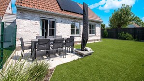 Una casa con techo de tejas, fachada de ladrillo y un patio con mesa y sillas.