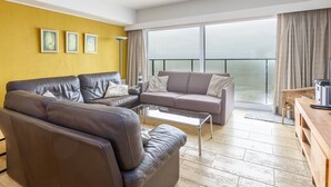 Un salon moderne avec un ensemble de canapés, une table basse et une vue sur la mer grâce à de grandes fenêtres.