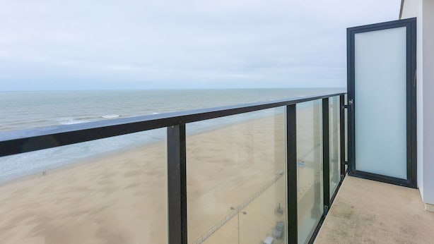 Un balcon doté d’une balustrade en verre, offrant une vue sur une plage et la mer.