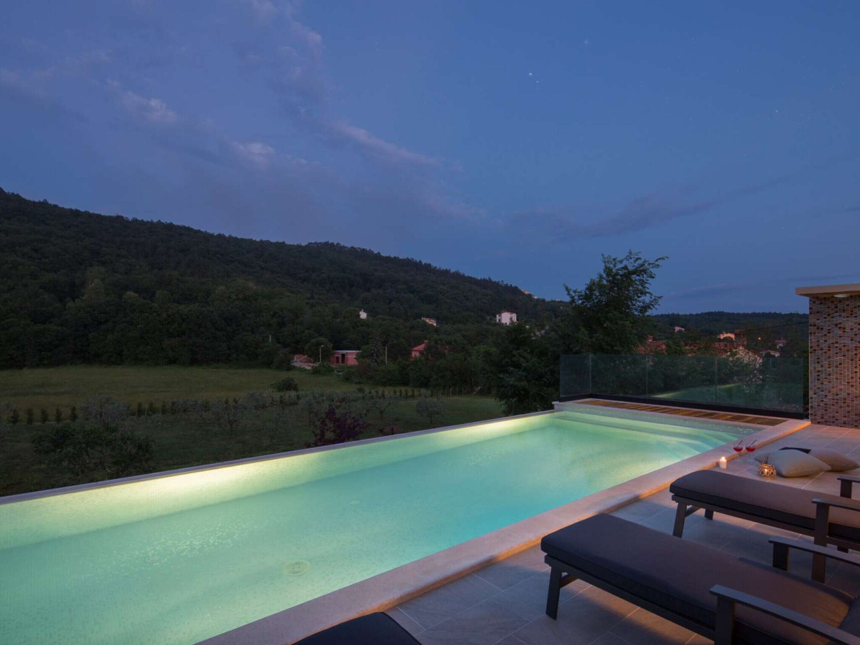 A swimming pool with lounge chairs and a view of a forested hillside.