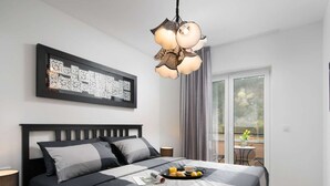 A modern bedroom with a large bed, a decorative light fixture, a framed artwork, and a view of the outdoors through a sliding glass door. - Villa With Pool Surrounded by Woods in Labin (Labin)