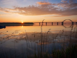 Un coucher de soleil sur un lac paisible, avec un pont en arrière-plan.