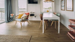 Una habitación con una mesa blanca, sillas de mimbre, un televisor montado en la pared y vista al agua.