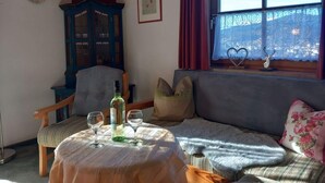 A cozy living room with a sofa, a table with a bottle and glasses, a cabinet, and a window with a view. - Hirschbichler Modern Retreat (Berchtesgaden)