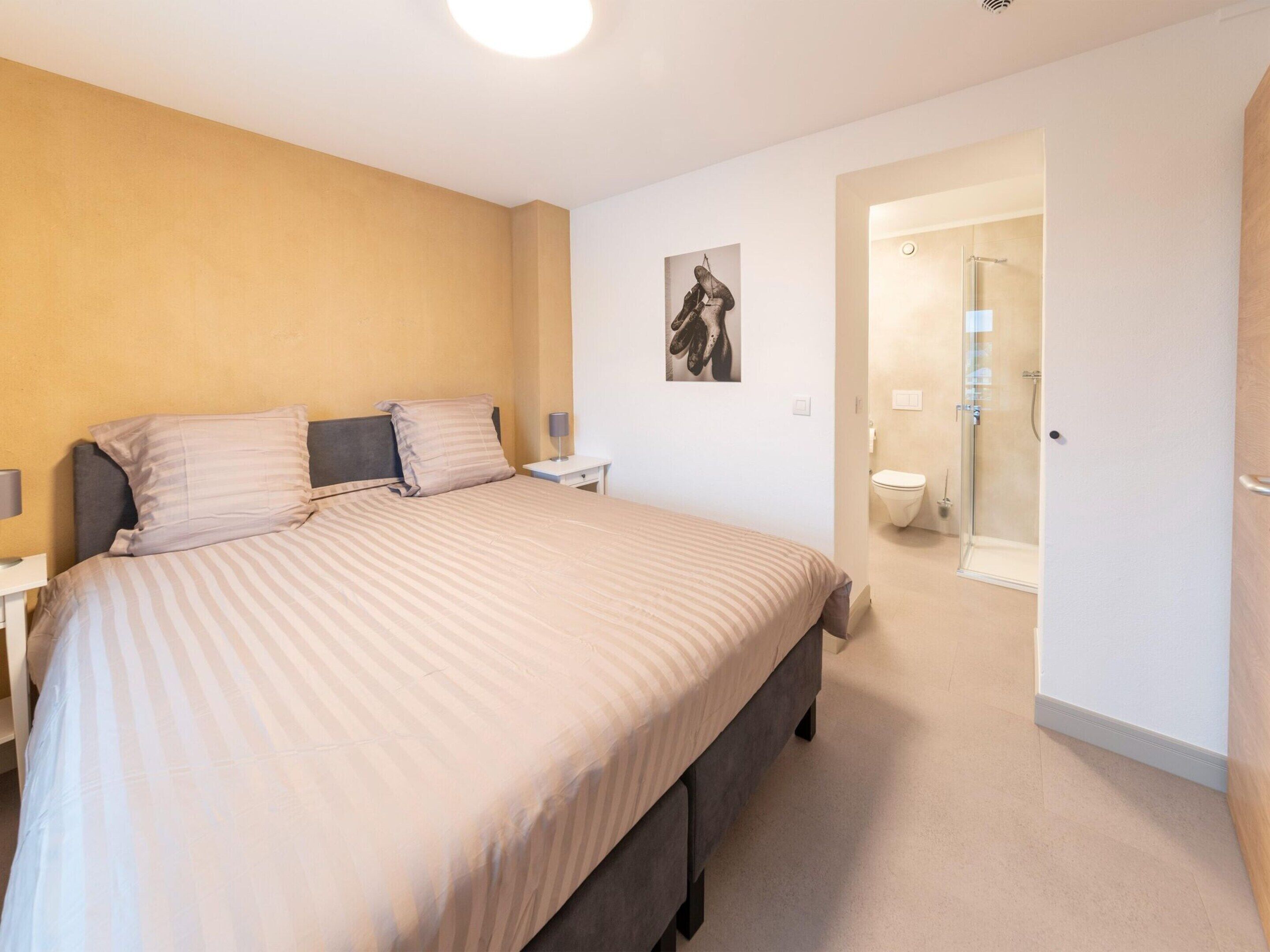 A bedroom with a bed, nightstands, a wall-mounted lamp, and a door leading to a bathroom.