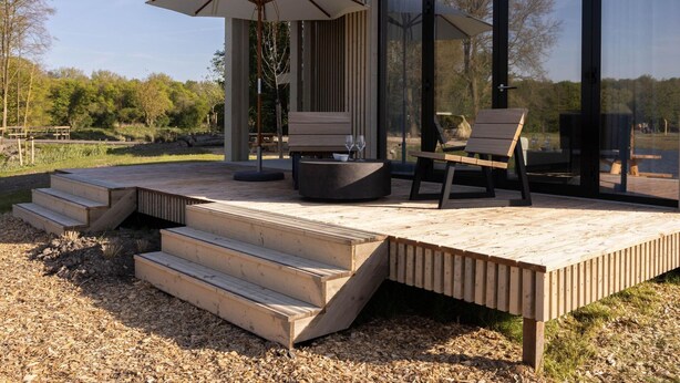 Una terrazza esterna moderna con gradini in legno, due poltrone, un tavolo e un ombrellone.