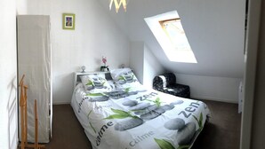 Un dormitorio con una cama y un edredón de temática 'Zen', una mesita de noche con lámpara, una ventana con vistas y una silla de madera.