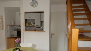 Un espacio habitable compacto con comedor, pequeña cocina y escalera de madera.