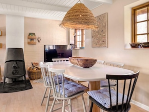 A dining area with a round table, white chairs, a woven hanging light fixture, a television, and a fireplace. - 5 Person Holiday Home in Nexo (Nexø)