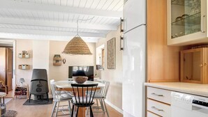 A modern kitchen with white cabinetry, a dining table with chairs, a hanging light fixture, and a built-in dishwasher. - 5 Person Holiday Home in Nexo (Nexø)