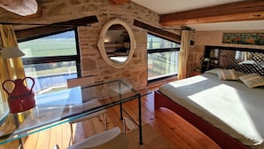 A rustic bedroom with a glass table, wooden beams, a stone wall, and a bed with pillows. - Villa Lucertole (Città di Castello)