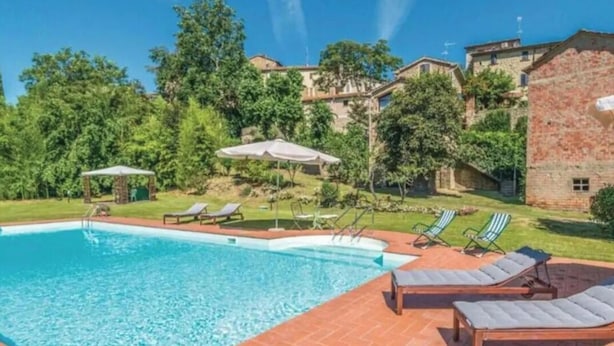 A swimming pool with lounge chairs and umbrellas, surrounded by greenery and buildings. - Villa Lucertole (Città di Castello)