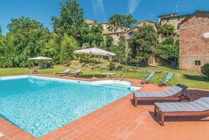A swimming pool with lounge chairs and umbrellas, surrounded by greenery and buildings. - Villa Lucertole (Città di Castello)
