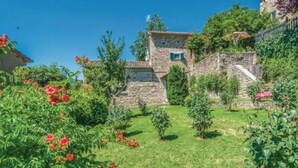 A stone building with a stone staircase, surrounded by lush greenery and flowering plants. - Villa Lucertole (Città di Castello)
