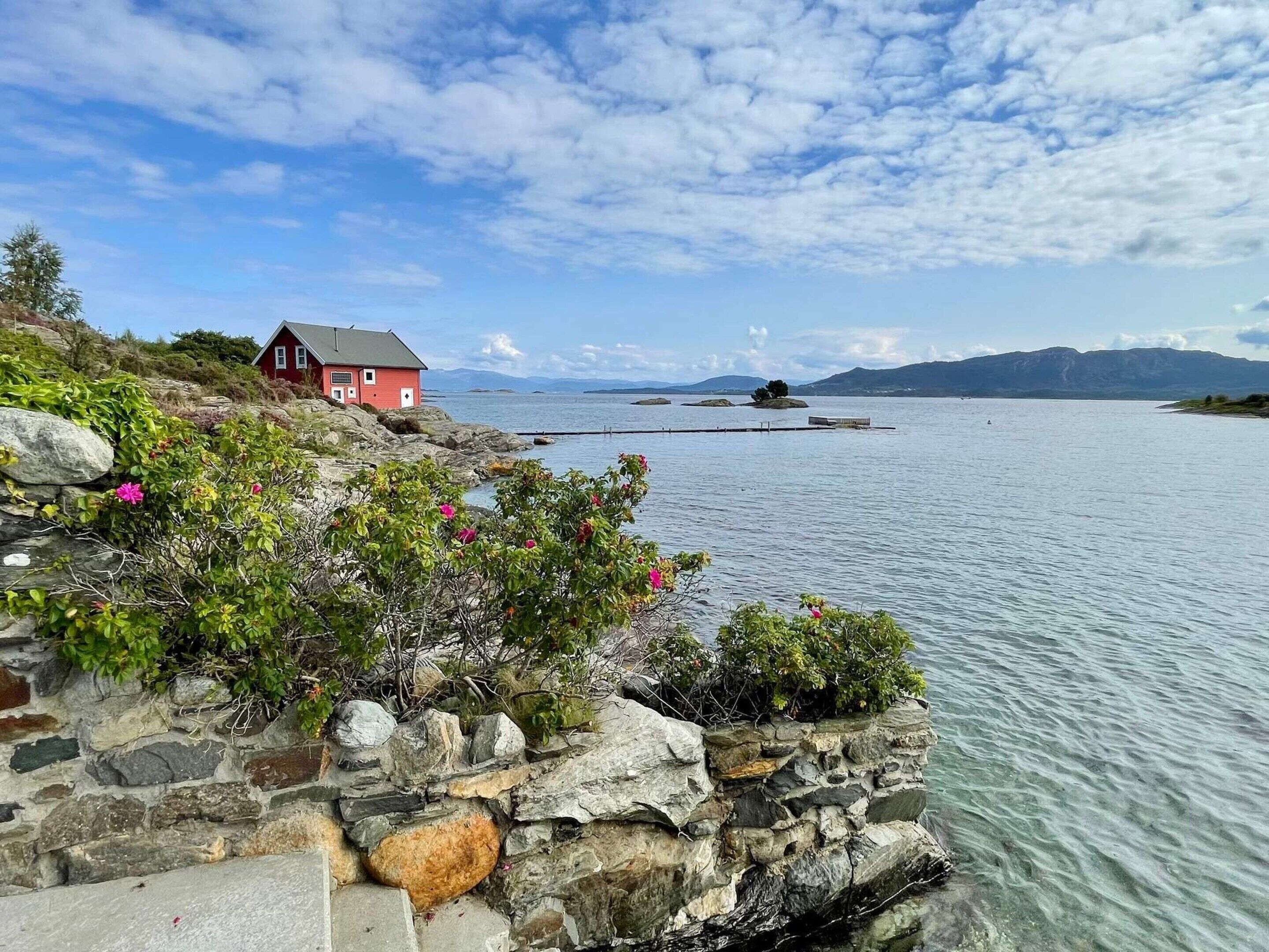 A stone wall with a red building and a dock extending into a calm lake.