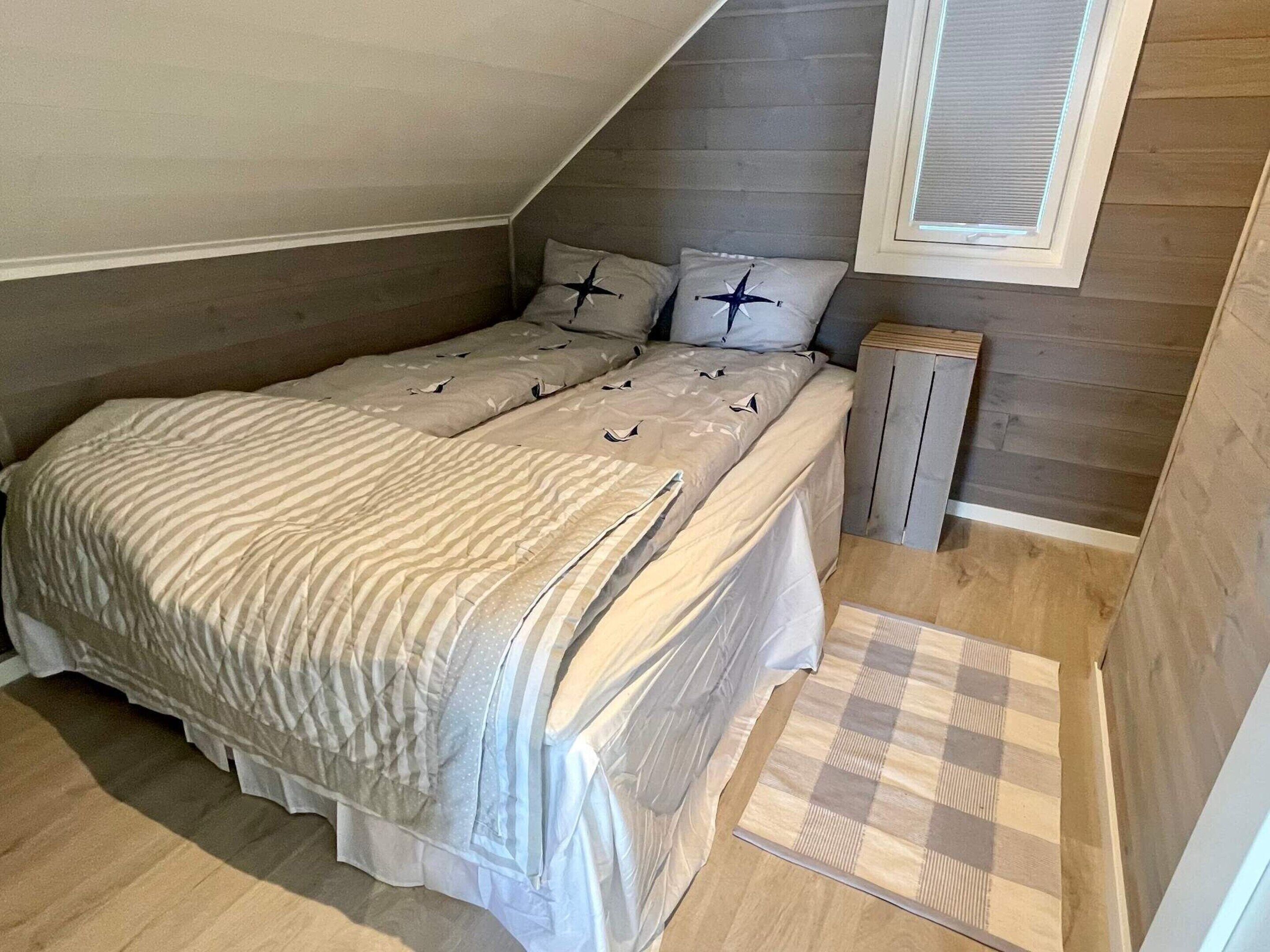 A small, cozy bedroom with a sloped ceiling, a bed with striped bedding, two pillows with star designs, and a small wooden nightstand.