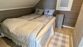 A small, cozy bedroom with a sloped ceiling, a bed with striped bedding, two pillows with star designs, and a small wooden nightstand.