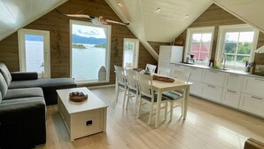 A cozy loft-style room with a dining area, kitchen, and a large window overlooking a body of water. - 4 Star Holiday Home in Mosterhamn-by Traum (Bomlo)
