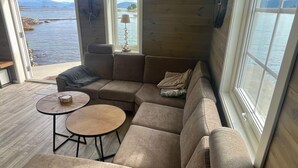 A modern living room with a sectional sofa, two round tables, and large windows offering a view of the sea. - 4 Star Holiday Home in Mosterhamn-by Traum (Bomlo)