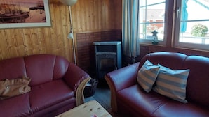 A cozy room with two red leather sofas, a small table, a fireplace, and a large window with curtains. - Holiday Home Villa Pippilotta (Userin)