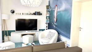 A living room with a large flat-screen TV, a white sofa, a decorative lamp, and a wall mural of a sailboat. - Seaside Apartment in Prerow (Ostseebad Prerow)
