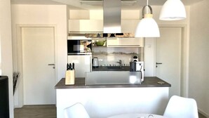 A modern kitchen with a central island, stainless steel appliances, and pendant lighting. - Seaside Apartment in Prerow (Ostseebad Prerow)