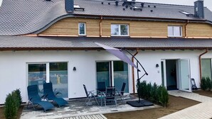 A two-story house with a sloped roof, large windows, and a patio area with outdoor furniture. - Seaside Apartment in Prerow (Ostseebad Prerow)