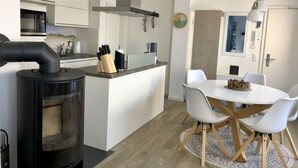 A modern kitchen with a central island, white dining table with chairs, and a wood-burning stove. - Seaside Apartment in Prerow (Ostseebad Prerow)