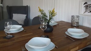 Een eettafel gedekt met witte borden, wijnglazen en een vaas met gele bloemen.