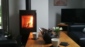 Een moderne woonkamer met een houtkachel, een flatscreen televisie en een eettafel met decoratieve objecten.