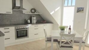 A modern kitchen with white cabinets, a built-in oven, and a dining area with a table and chairs. - Apartment Achtern Meer II (Boergerende-Rethwisch)