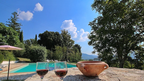 Escena junto a la piscina con una mesa que presenta copas de vino, manzanas y una maceta de barro.