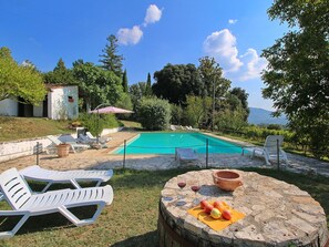 Un patio trasero con piscina, sillas de descanso y una mesa con fruta y copas de vino.