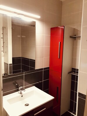 A bathroom with a white sink, a red cabinet, and black and white tiled walls. - Accès Direct Mer, Appartement Pour 6 Personnes (Arzon)