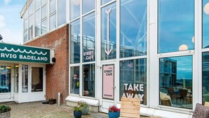 A street cafe with a modern glass facade, outdoor seating with wooden tables and chairs, and a sign indicating 'Take Away' service. - 6 Person Holiday Park Home in Ringkobing (Ringkobing)