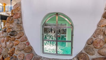 A stone wall with a window featuring a green frame and a view of a green building outside.