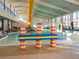 An indoor swimming pool with colorful barriers, a stone wall, and a view of the outside through large windows.