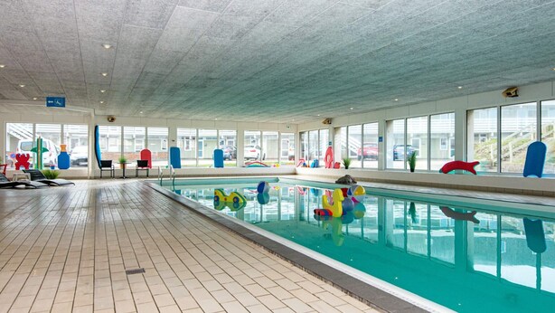 An indoor swimming pool with a tiled floor, clear glass walls, and colorful pool toys. - 6 Person Holiday Park Home in Ringkobing (Ringkobing)