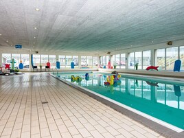 Una piscina interior con suelo de baldosas, paredes de vidrio transparente y juguetes de colores.