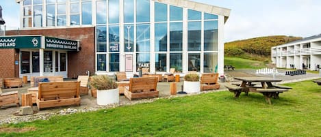 A modern building with large windows, outdoor seating, and a chess table.