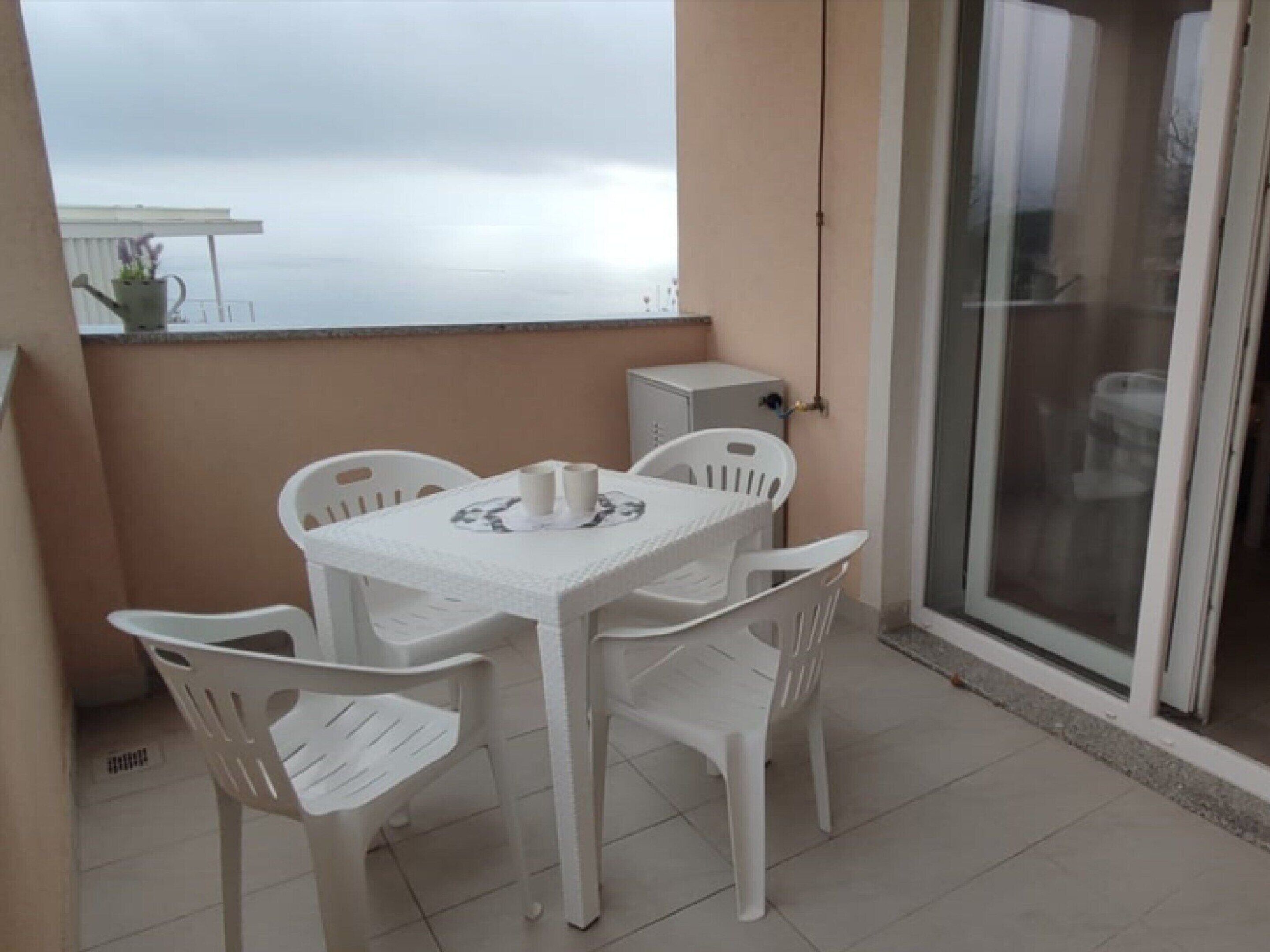 Un petit balcon avec une table et des chaises, une plante en pot et une vue sur la mer.
