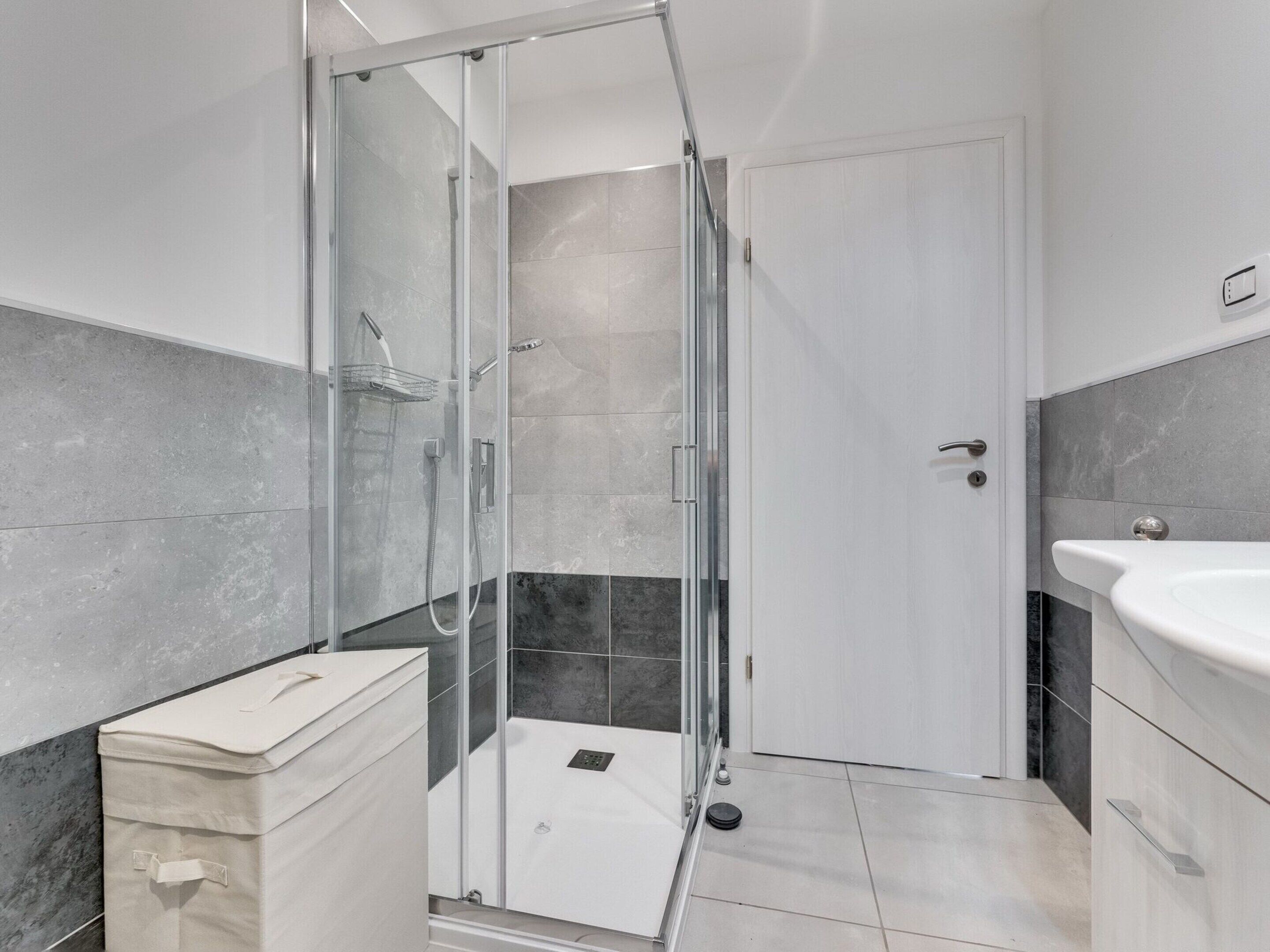 A modern bathroom with a glass shower enclosure, a white sink, and a marble-tiled floor.