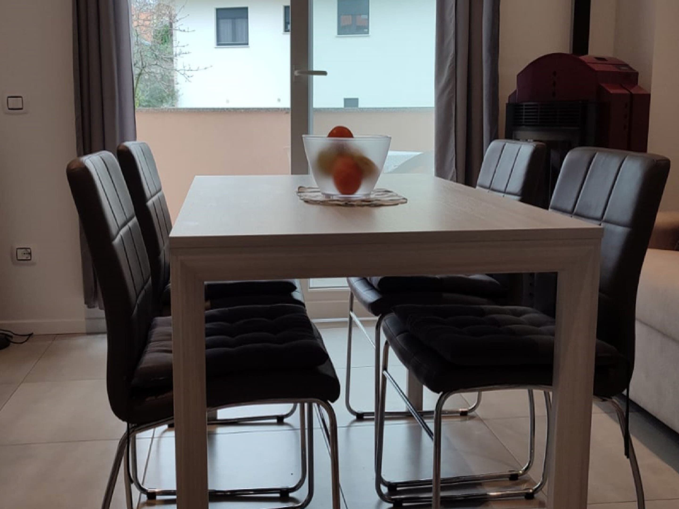 Un comedor con una mesa blanca, sillas tapizadas en negro y un tazón de vidrio sobre la mesa.