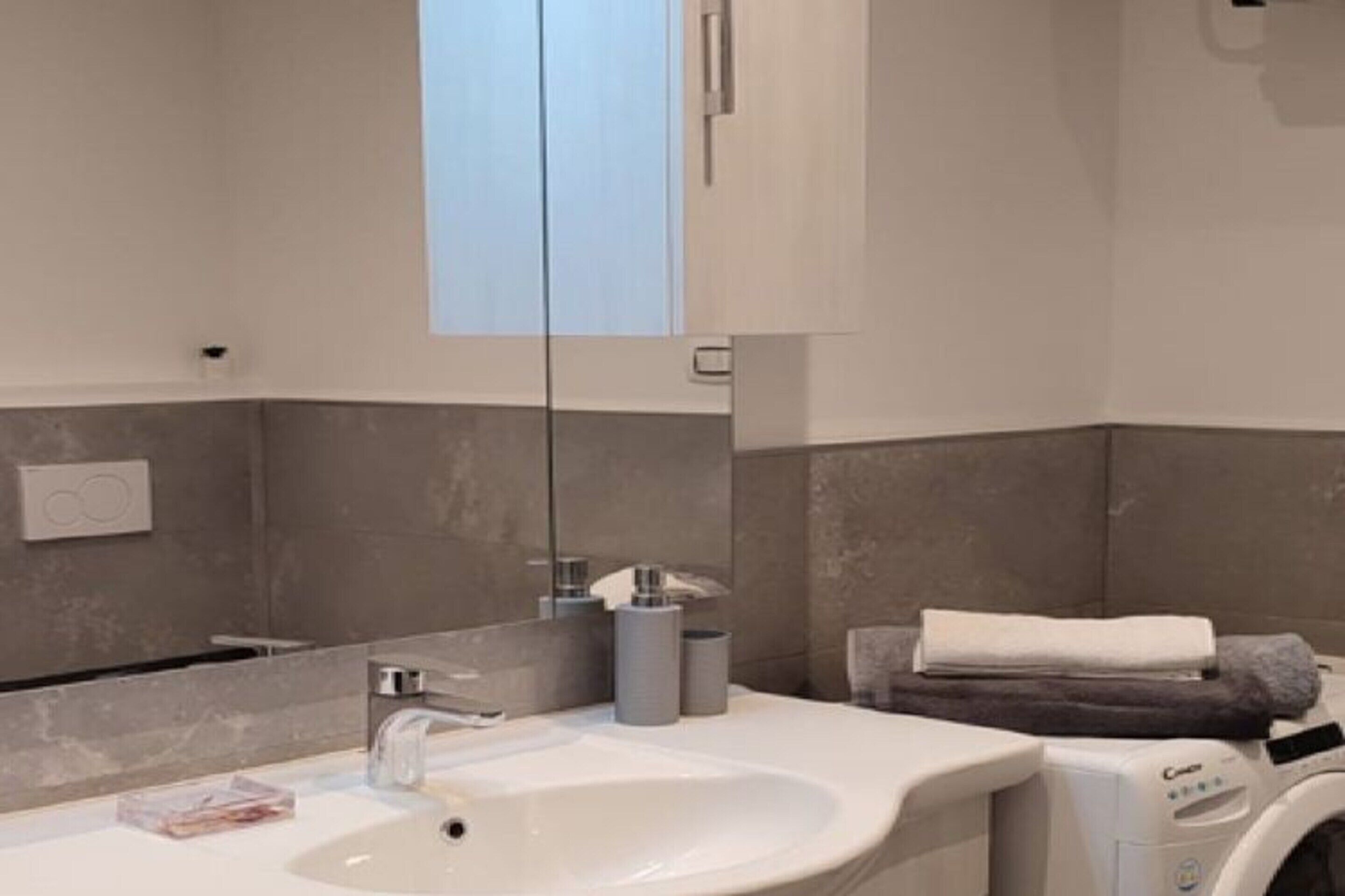 Une salle de bain moderne avec un lavabo blanc, un miroir, un porte-serviettes et un lave-linge.
