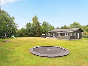 A residential property with a house, a trampoline, and a swing set in a grassy yard.