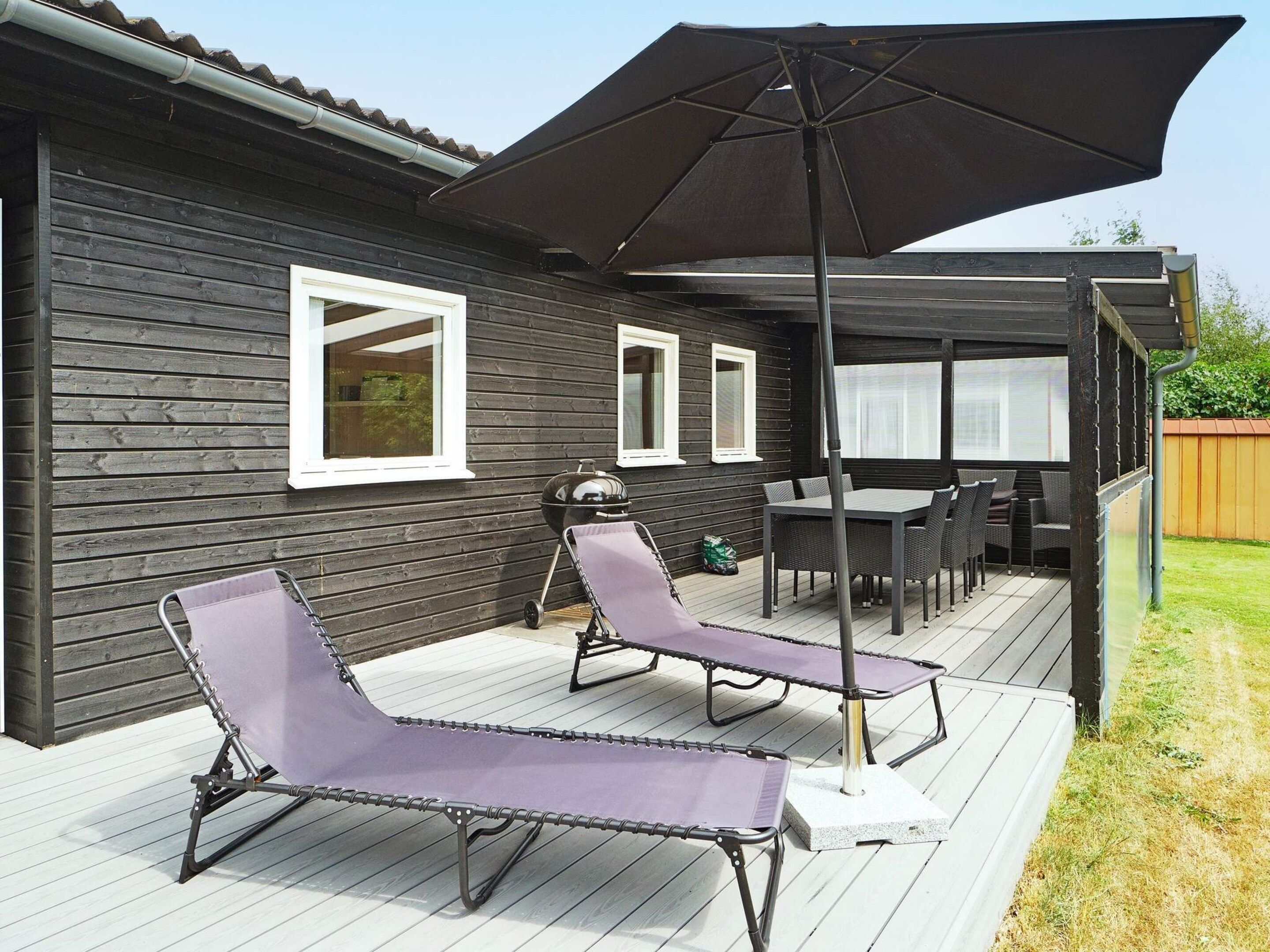 A deck with lounge chairs and a table, a barbecue grill, and a large umbrella.